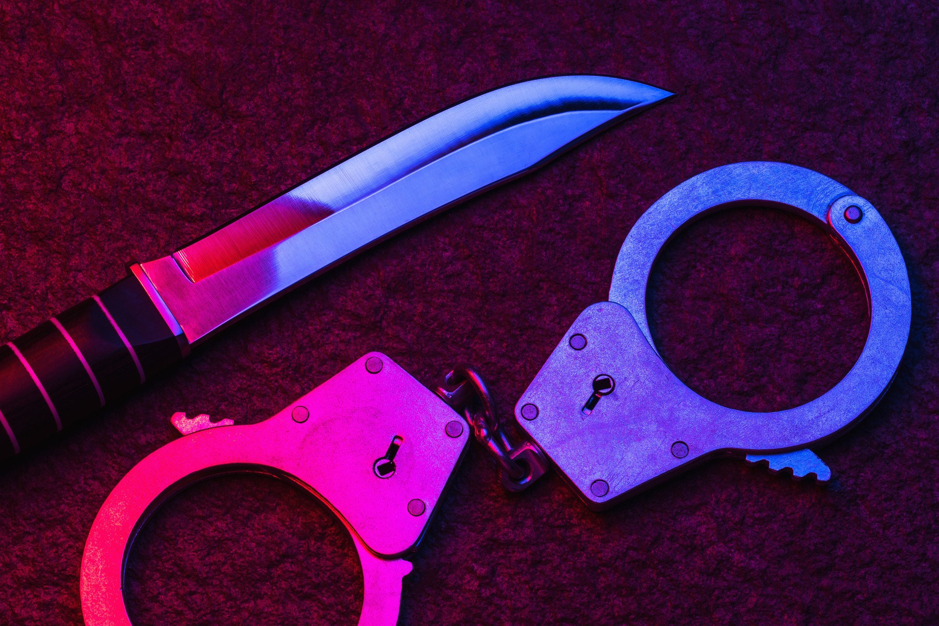 Handcuffs and a knife on a stone surface illuminated by the flashing lights of a police car. Concept on the topic of punishment for a committed crime