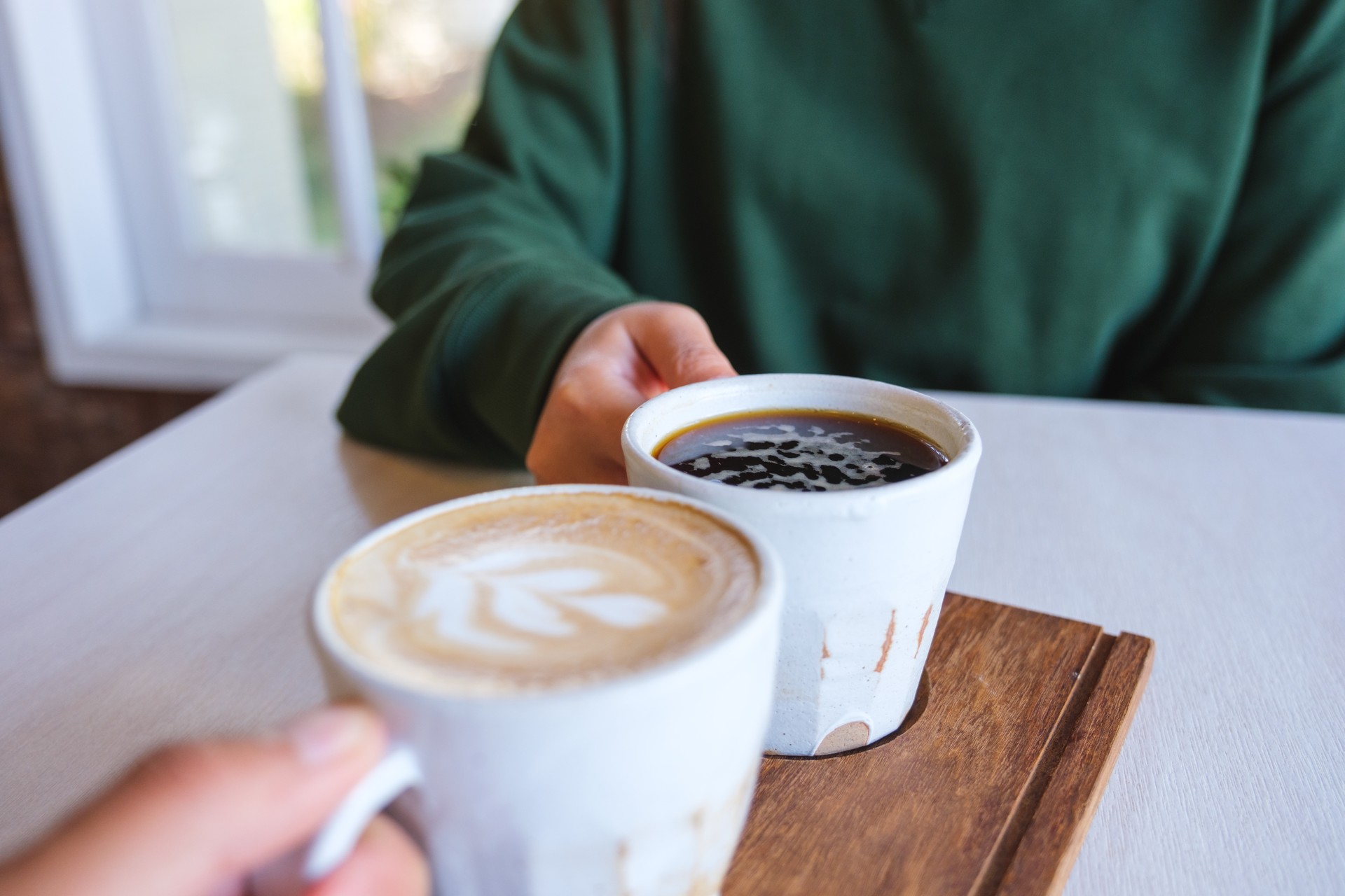 Closeup image of a couple people holding and clinking coffee cups together in cafe