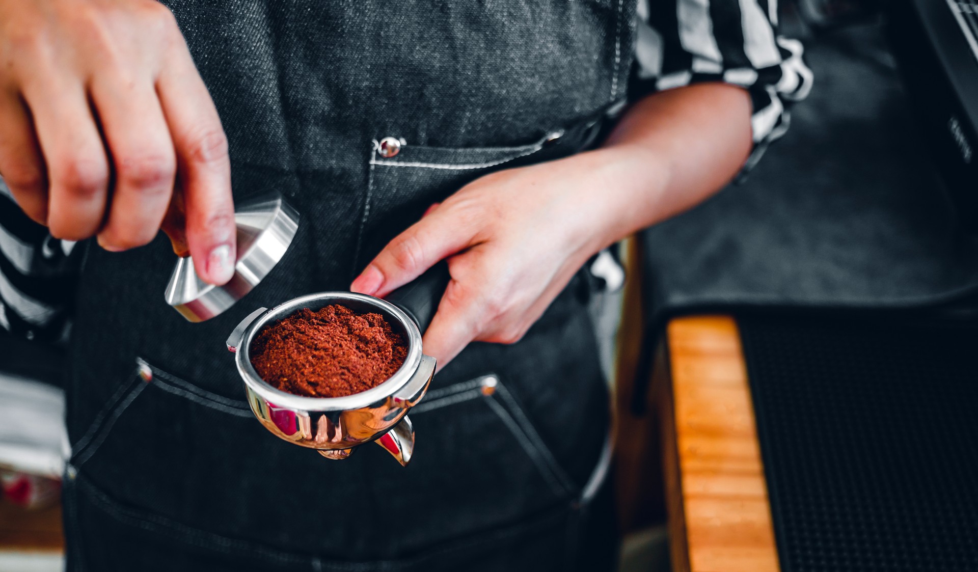 Barista holding portafilter and coffee tamper making an espresso coffee in cafe