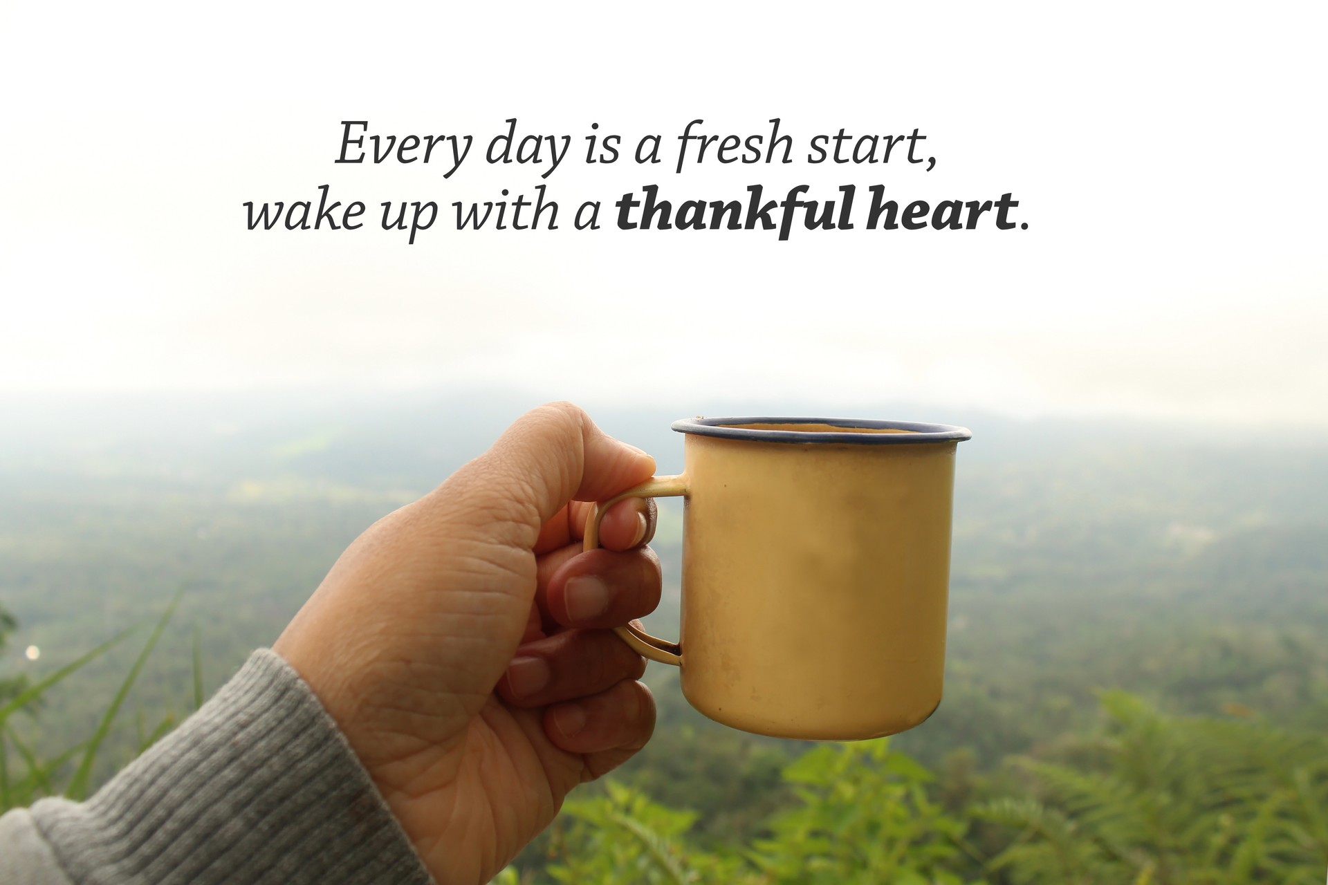 Person holding yellow cup of tea or coffee in hand against mountain view with a morning thankful inspirational message.